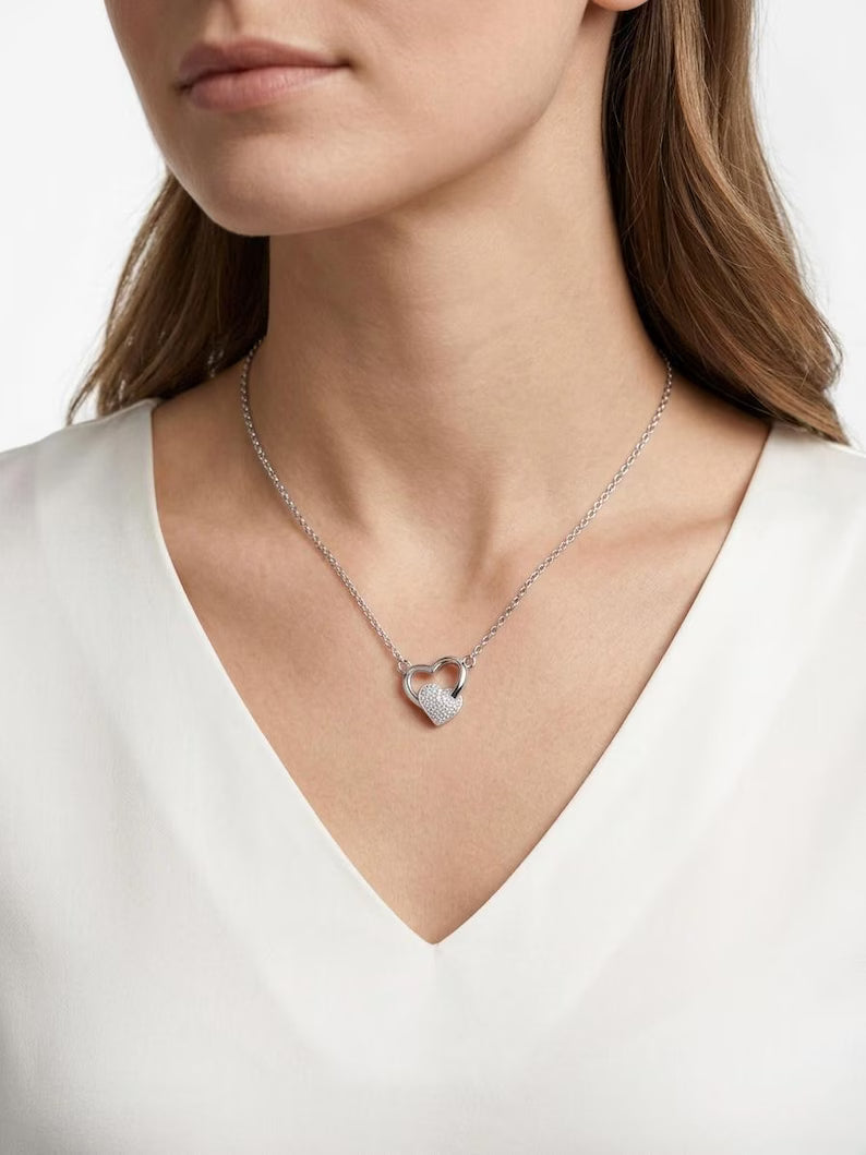 A close-up of a woman wearing a delicate silver heart-shaped pendant necklace with a textured, glittering finish, paired with a white V-neck top.