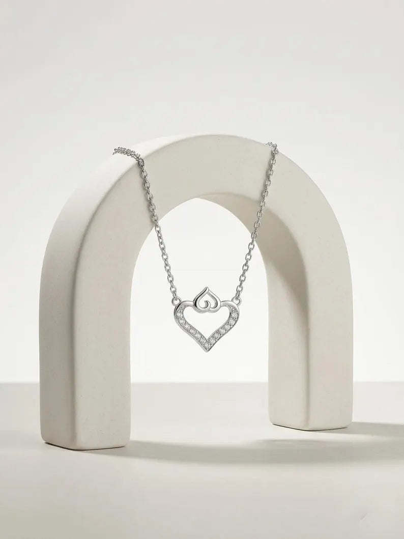 A silver heart-shaped pendant necklace with a small interlocking hearts design, displayed on a white arch stand against a clean white background.