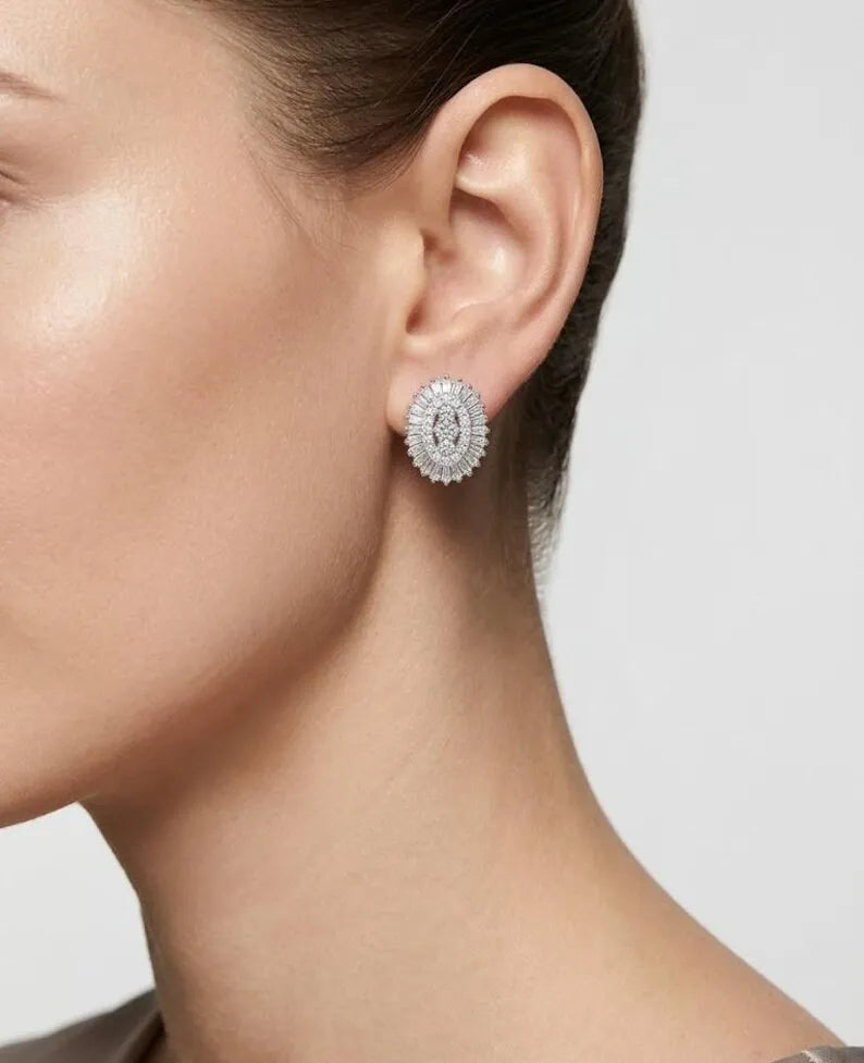 A close-up side profile of a model wearing a silver-toned oval stud earring encrusted with clear gemstones.