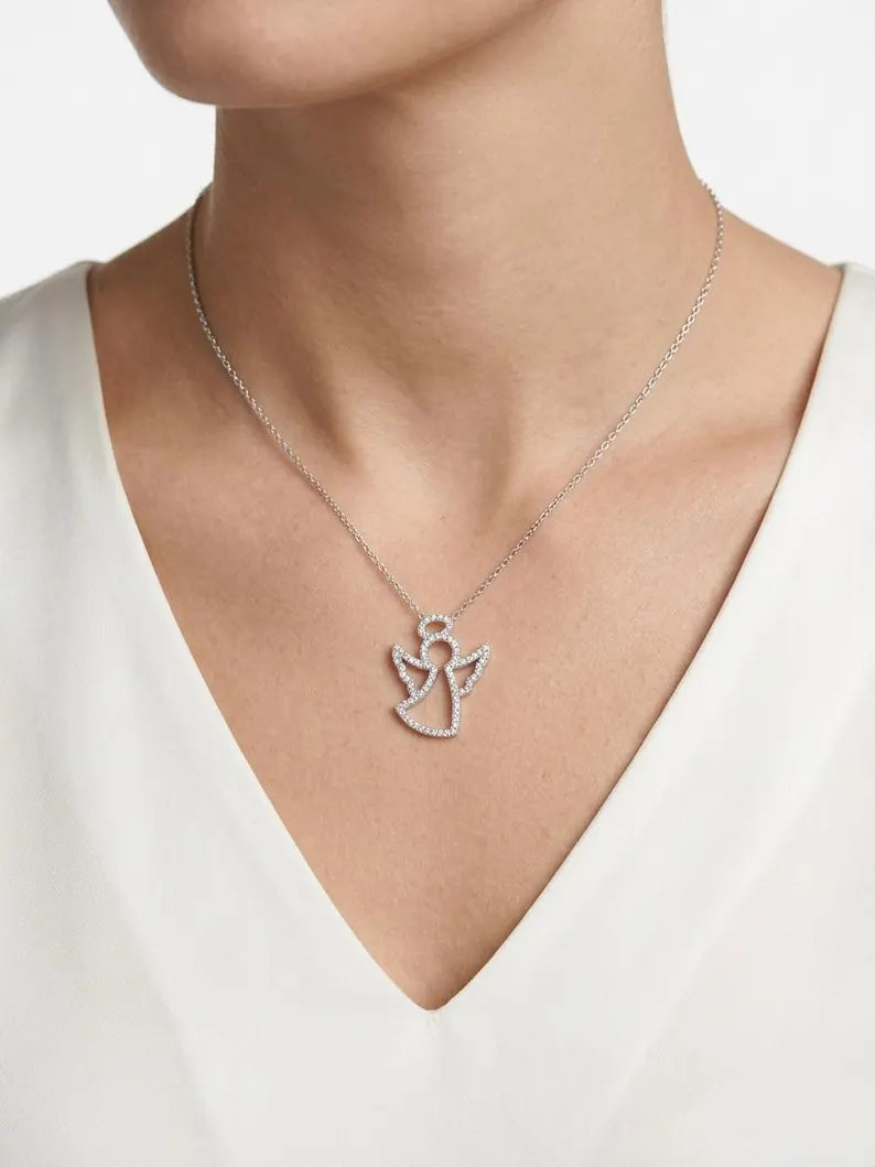 A close-up of a model wearing a delicate silver angel pendant necklace on a fine chain, styled with a white V-neck top against a clean white background.