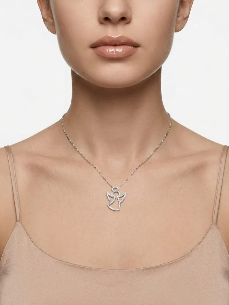 A close-up of a model wearing a delicate silver angel pendant necklace on a fine chain, paired with a beige camisole top against a clean white background.
