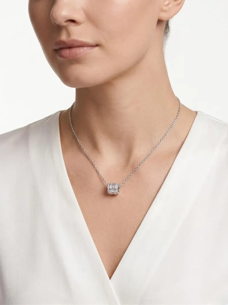 A close-up of a model wearing a delicate silver chain necklace with a square-cut clear gemstone pendant, styled with a white V-neck top.