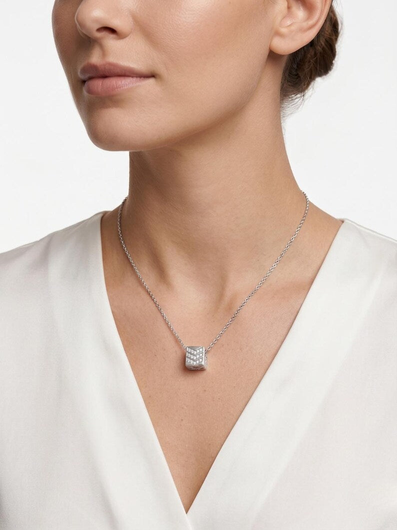 A close-up of a woman wearing a delicate silver chain necklace with a small square pendant paved with clear stones, paired with a white V-neck top.