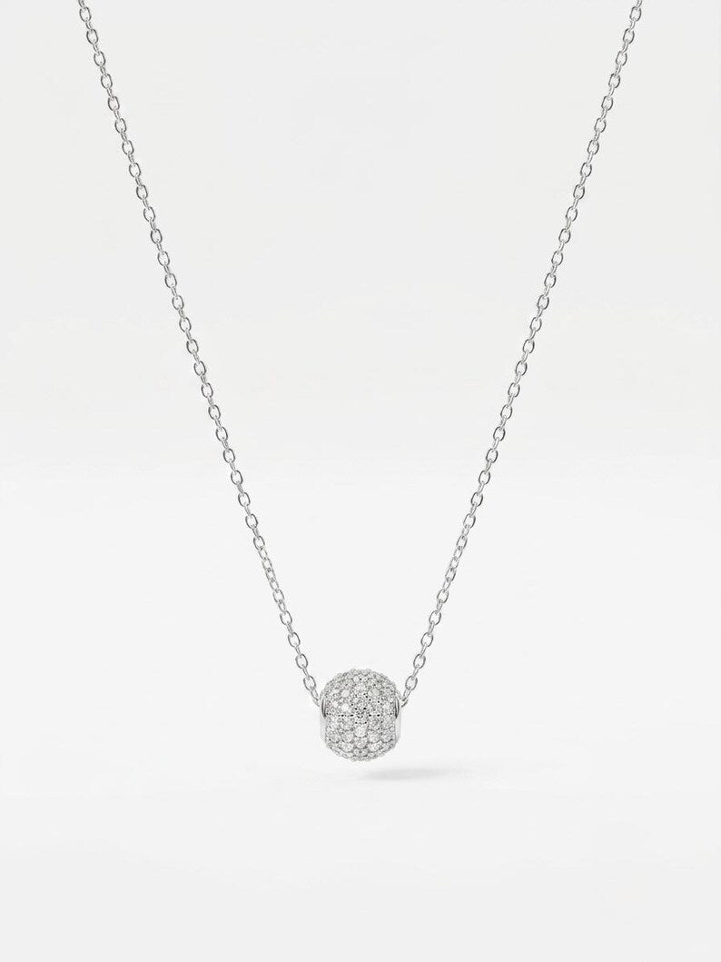 A delicate silver chain necklace featuring a small, round pavé-set pendant with clear stones, displayed against a clean white background.