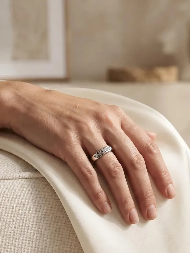 Hand resting on cream fabric wearing a wide sterling silver band ring with channel-set CZ panels