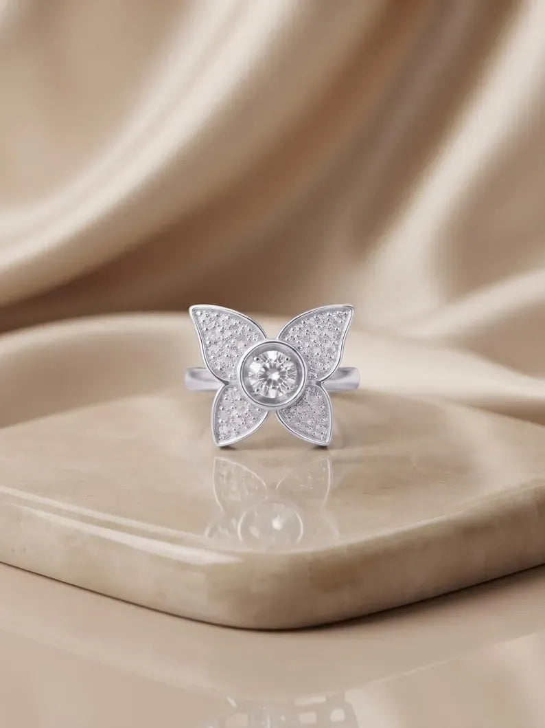 Four-petal CZ flower ring displayed on a marble tray with beige silk fabric in the background