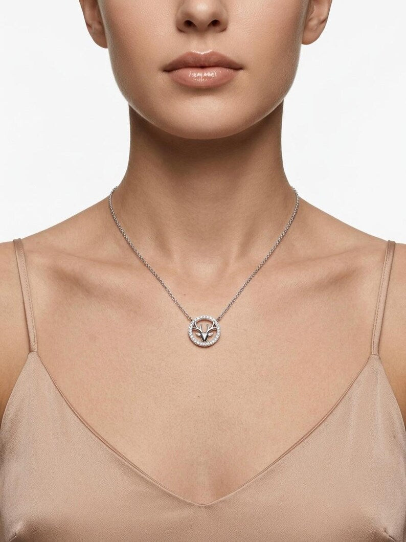 A close-up of a model wearing a delicate silver chain necklace with a circular pendant featuring a stylized bird or fox head, set against a clean white background.
