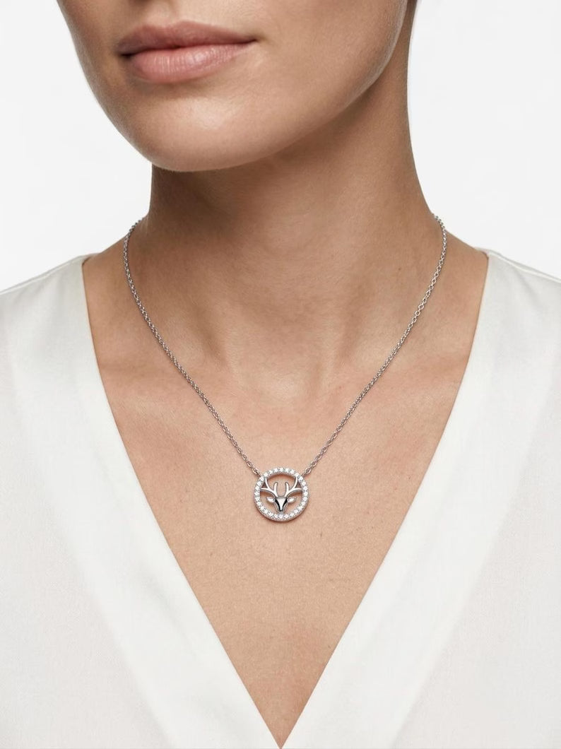 A close-up of a model wearing a delicate silver chain necklace with a circular pendant featuring a tree of life design surrounded by small clear stones, paired with a white V-neck top.