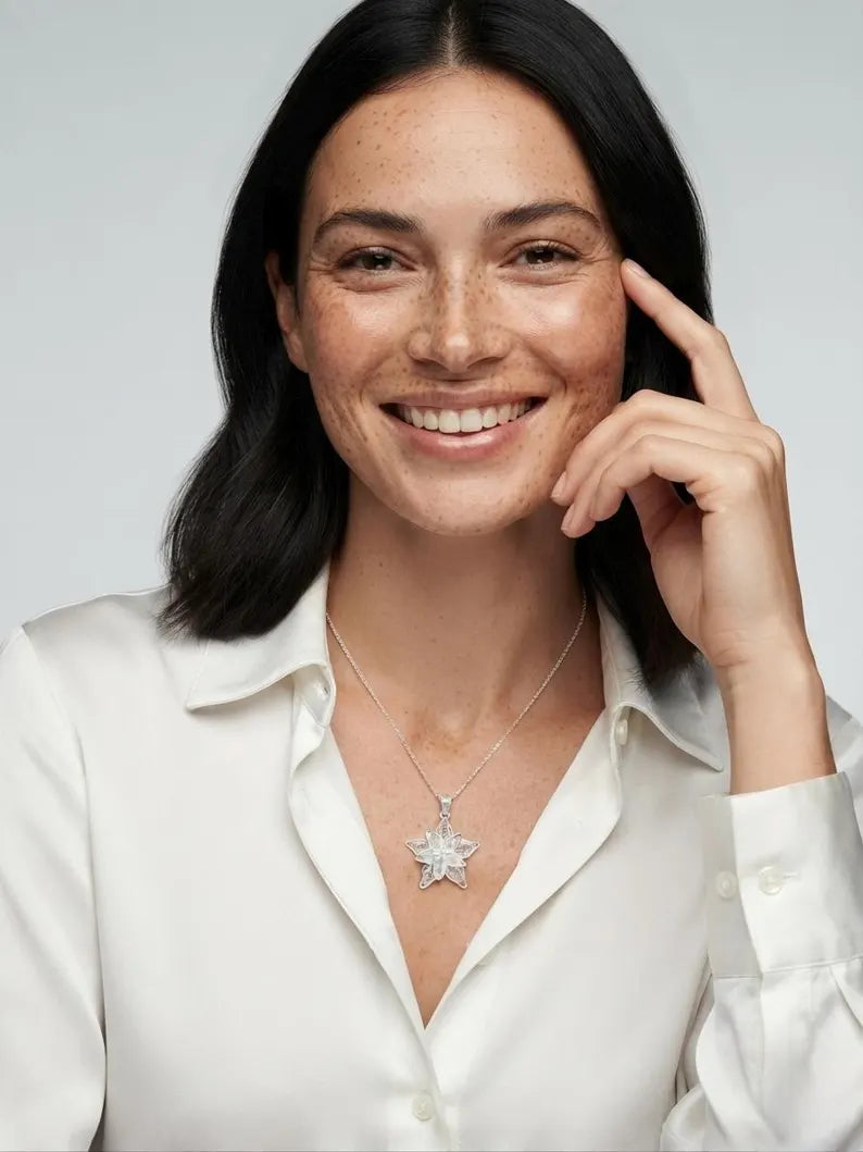 A smiling woman with dark hair wears a white collared shirt and a silver star-shaped pendant necklace against a light gray background.