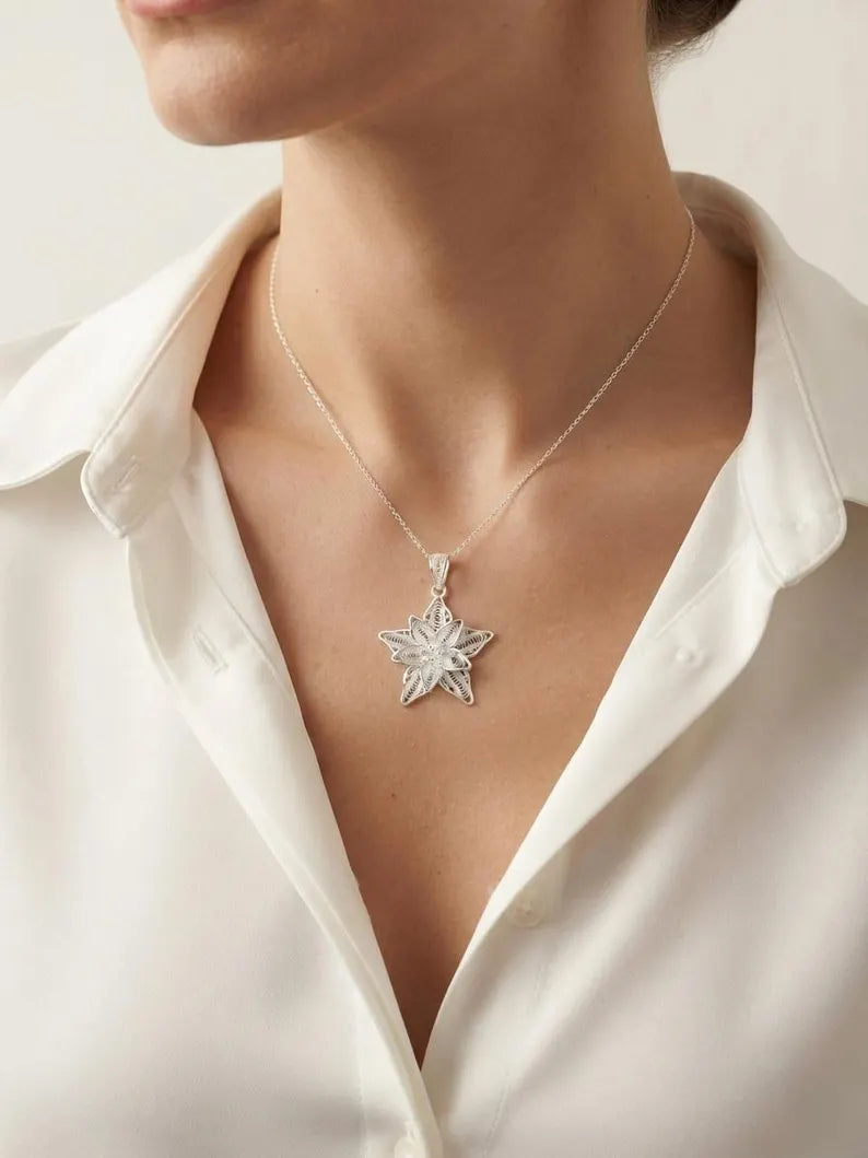 A silver-toned starburst pendant necklace worn by a model in a white collared blouse, shown in a close-up shot.