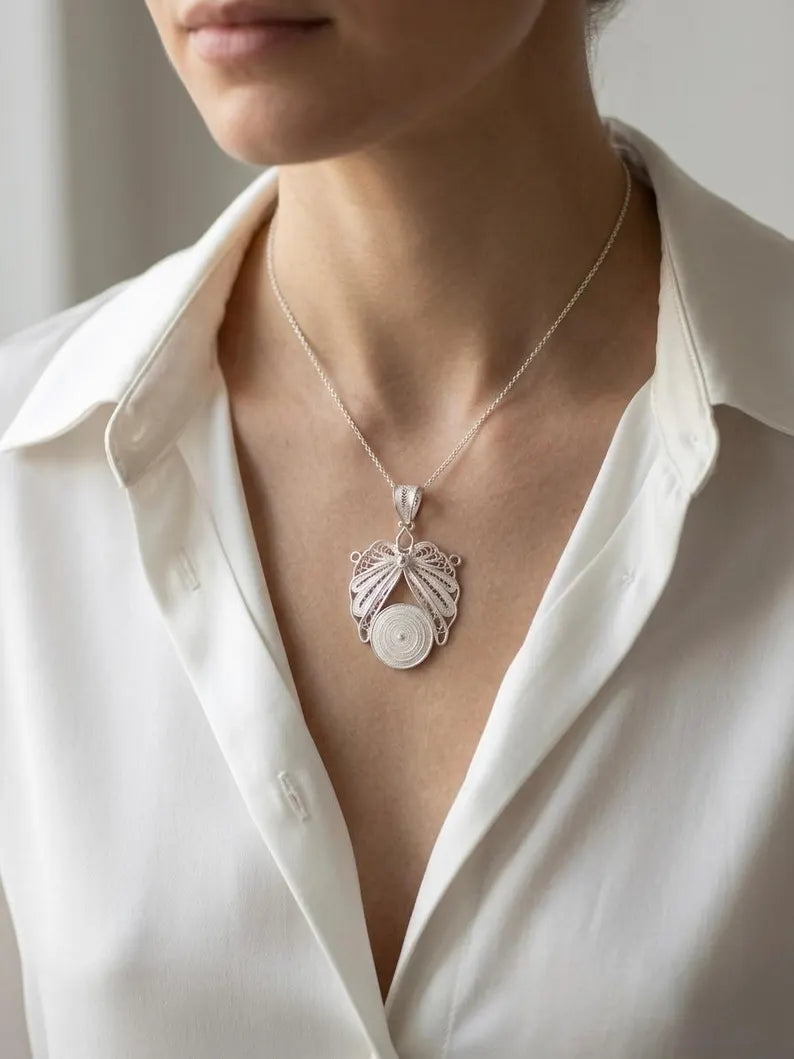 A close-up of a woman wearing a delicate silver pendant necklace with a circular white stone, styled with a white button-down shirt.