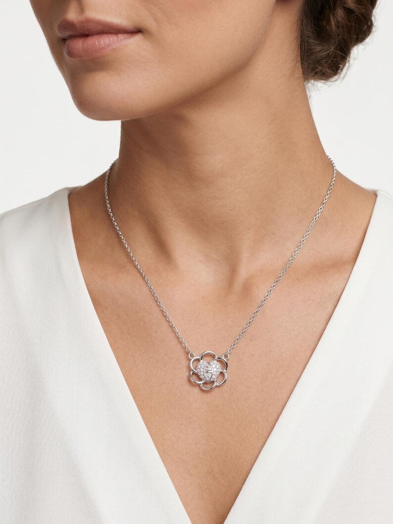 A close-up of a model wearing a delicate silver chain necklace with a flower-shaped pendant featuring a clear central gemstone and small clear side stones, paired with a white V-neck top.
