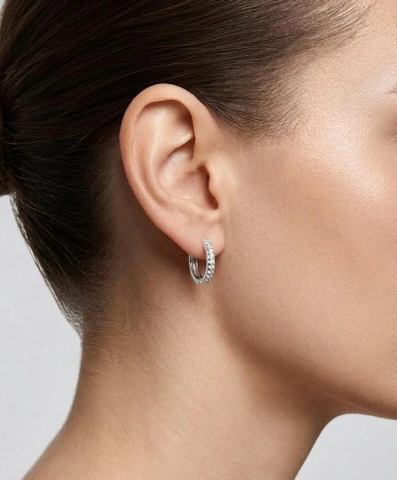 A close-up of a model's ear wearing a small silver hoop earring with a textured pavé setting.