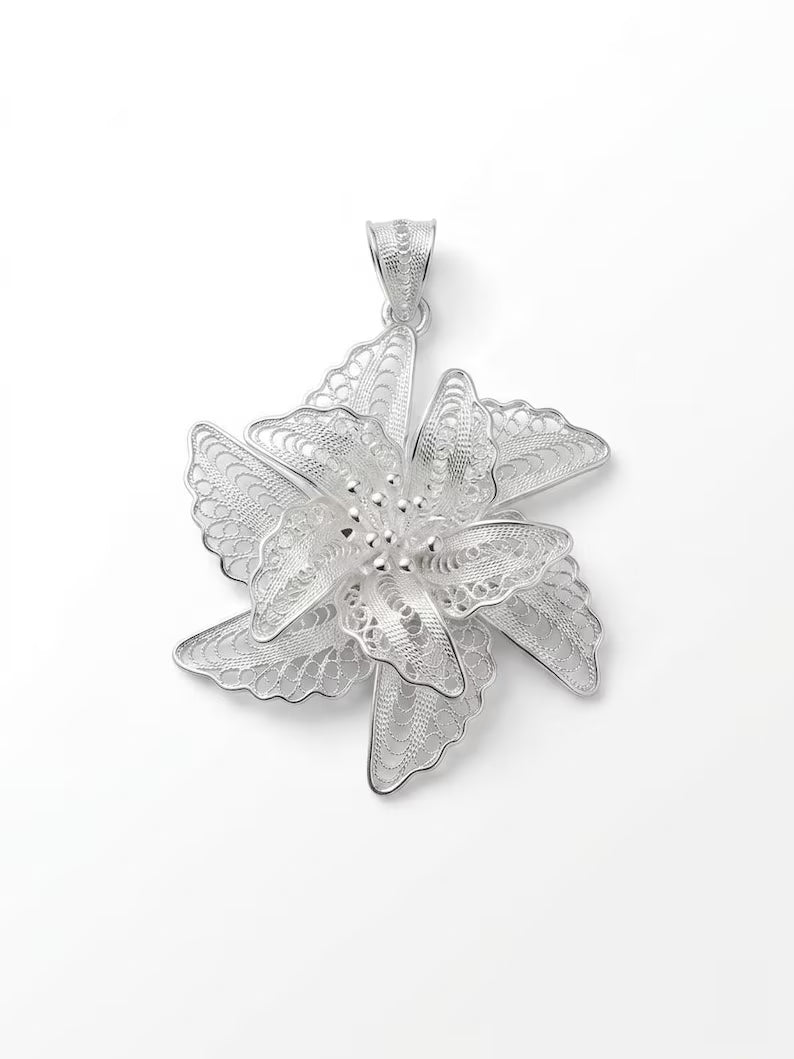 A silver-toned filigree pendant shaped like a six-petal flower, photographed against a clean white background.