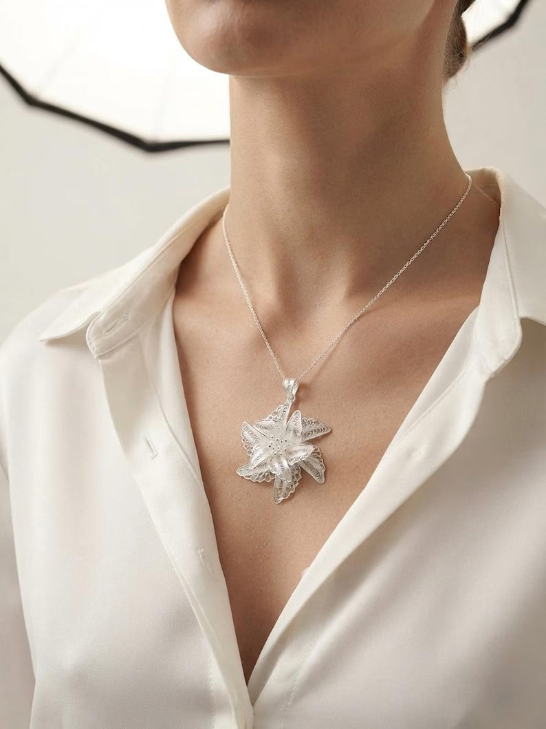 A close-up of a model wearing a silver-toned starburst pendant necklace with clear crystals, styled with a white satin shirt.