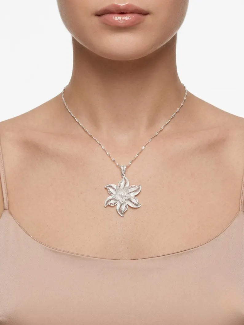 A silver-toned flower-shaped pendant necklace worn by a model, shown from the neck to the upper chest against a clean white background.