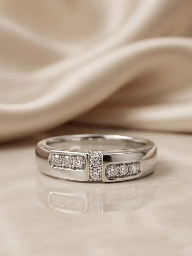 Angled view of a polished sterling silver band ring with CZ channel setting, resting on beige fabric