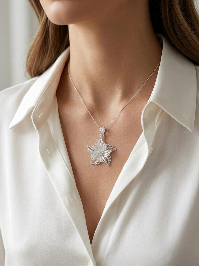 A close-up of a model wearing a silver starfish pendant necklace with a textured, hammered finish, styled with a white collared blouse.