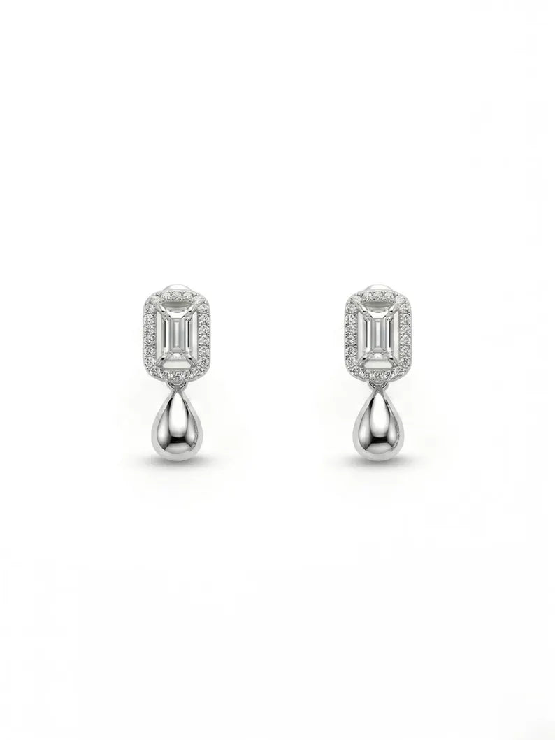 A pair of silver-toned drop earrings featuring baguette-cut clear gemstones in a halo setting with a polished teardrop drop below, shown on a plain white background.