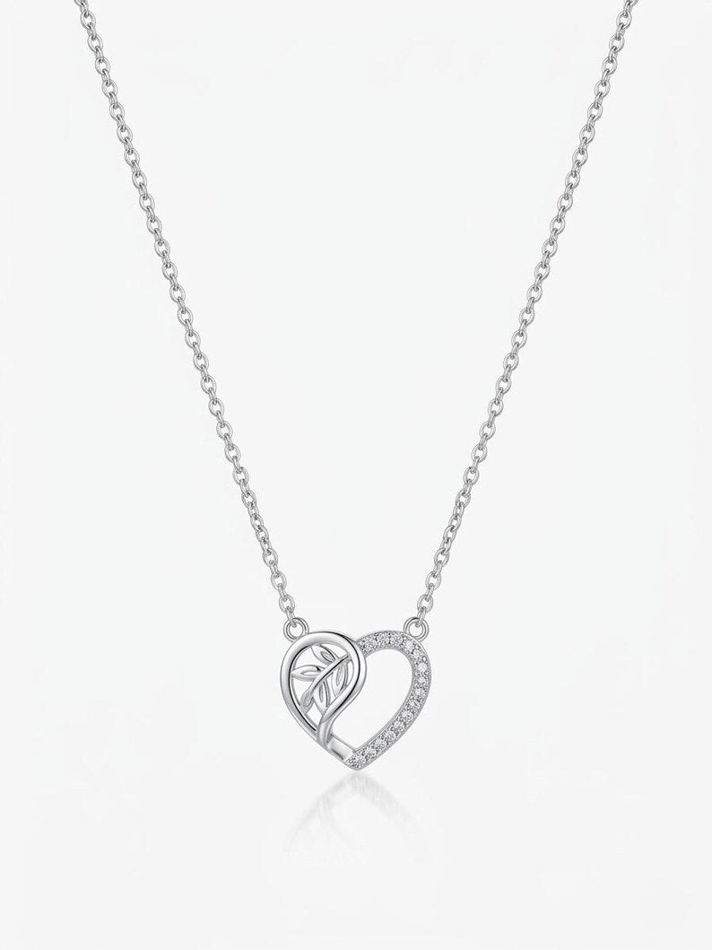 A silver heart-shaped pendant necklace with a small leaf motif inside one half of the heart and a row of clear stones along the outer edge, shown on a delicate silver chain against a light gray background.