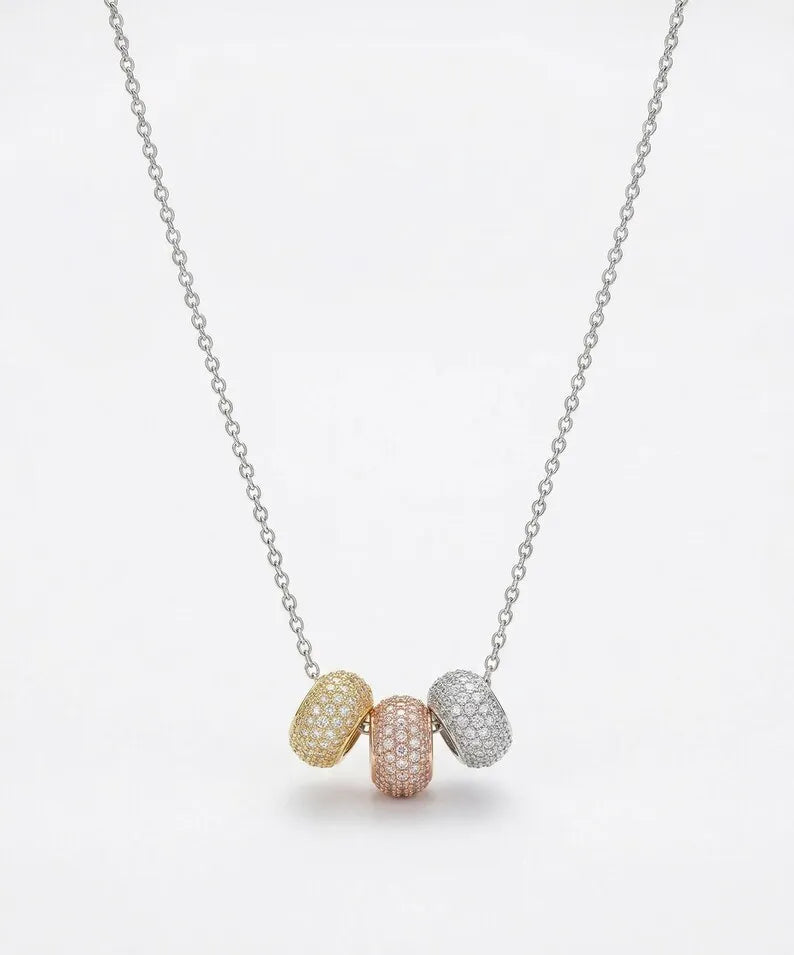 A delicate silver chain necklace featuring three small, oval pavé-set beads in yellow gold, rose gold, and white gold, displayed against a clean white background.
