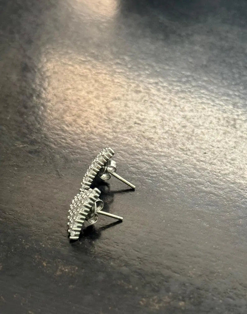 A pair of silver-toned textured stud earrings with small clear stones, shown on a dark, reflective surface.