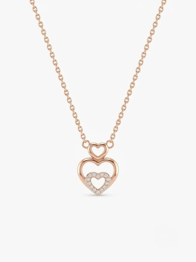 A rose gold necklace with a double heart pendant, featuring a larger open heart and a smaller heart paved with clear stones, shown on a light gray background.