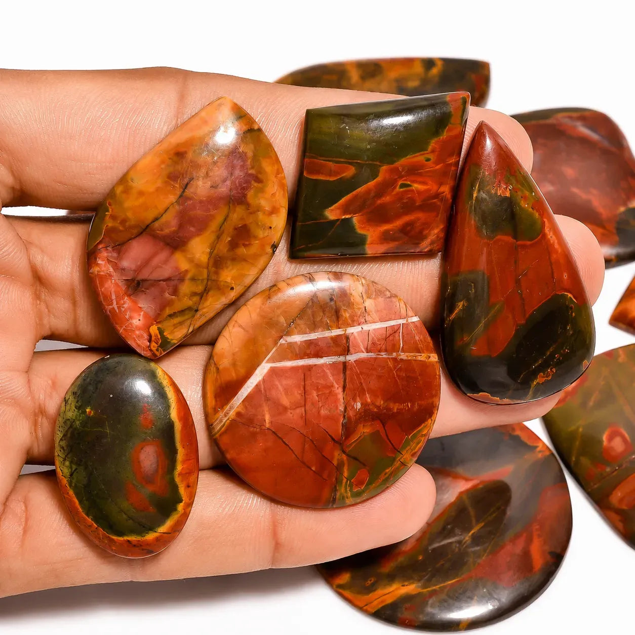 Hand holding various red and green marbled stones against a white background