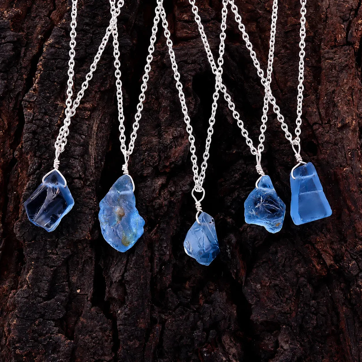 Five blue stone pendants on silver chains against a dark wooden background