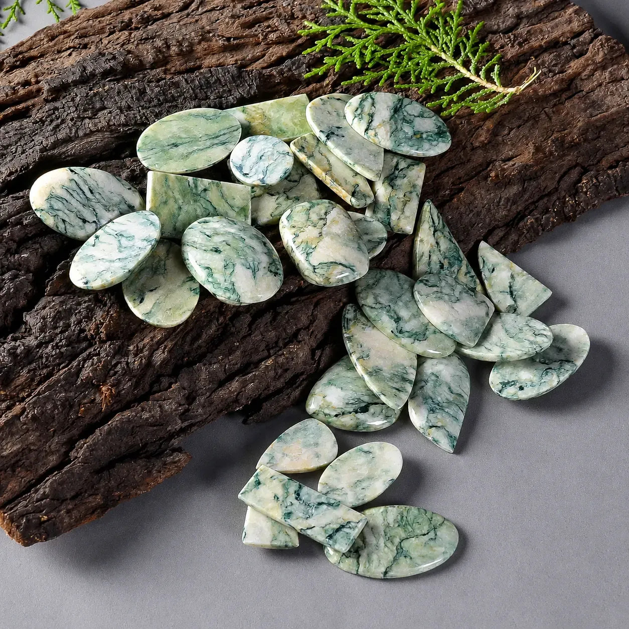 Green marbled stones on a gray surface with wooden logs and greenery