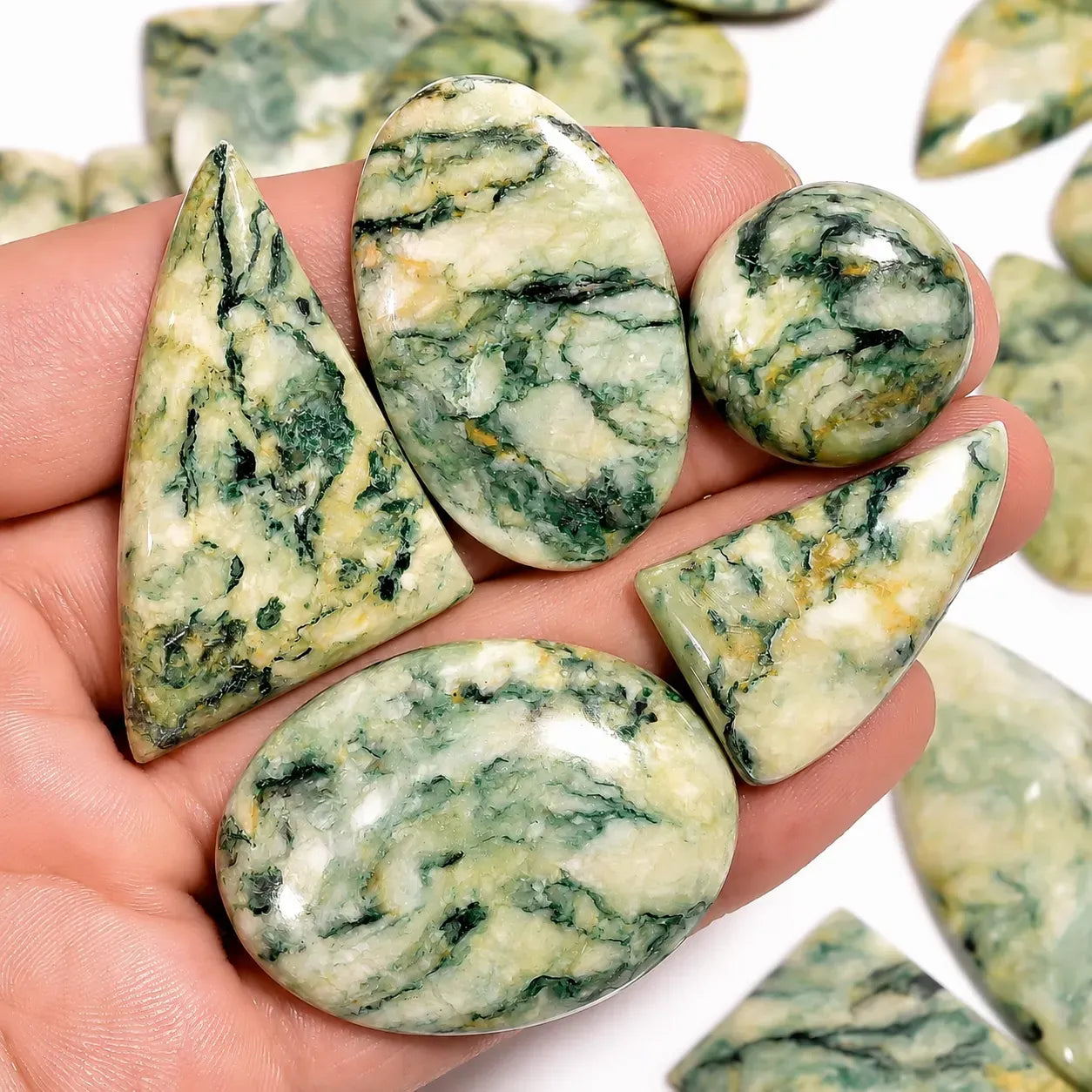 Hand holding green and white marbled stones with more stones in the background