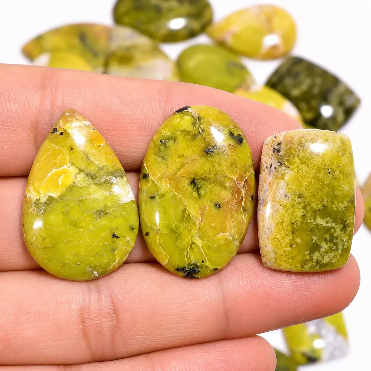 Three greenish-yellow stones held between fingers with a blurred background of more stones.