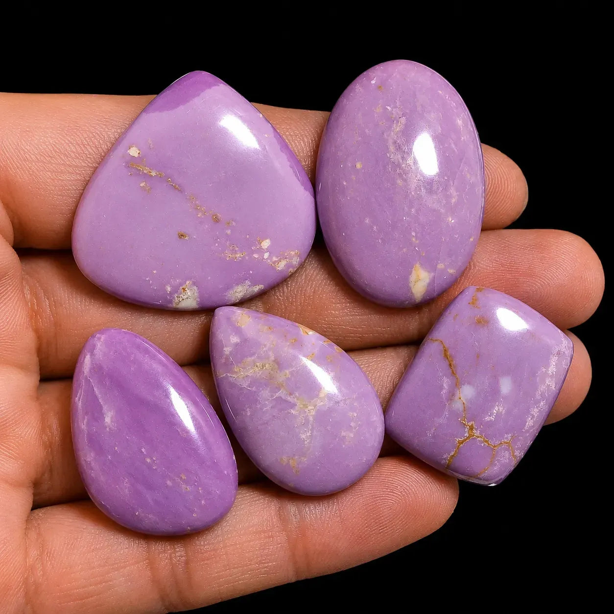 Five purple stones with gold veins held in a hand against a black background