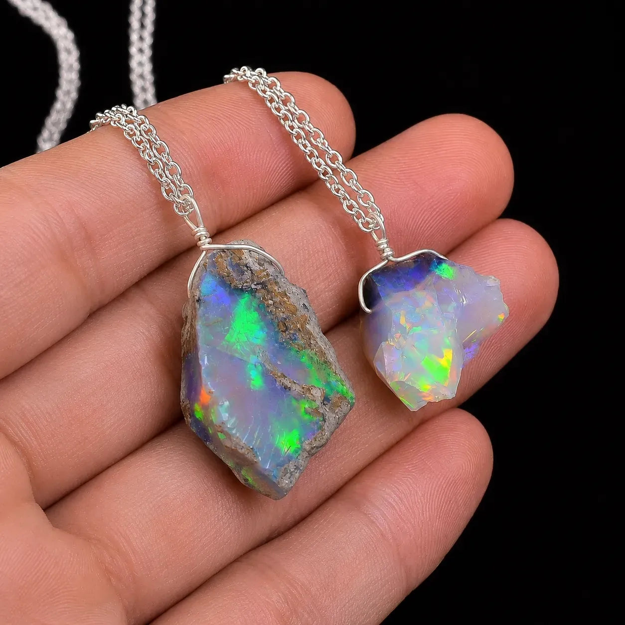 Opal pendants on silver chains held in a hand against a black background